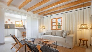 A modern living room with a sofa, two armchairs, a coffee table, and a dining area. There is a kitchen visible in the background. - Villa Can Canavaret by SunVillas Mallorca (Pollença)