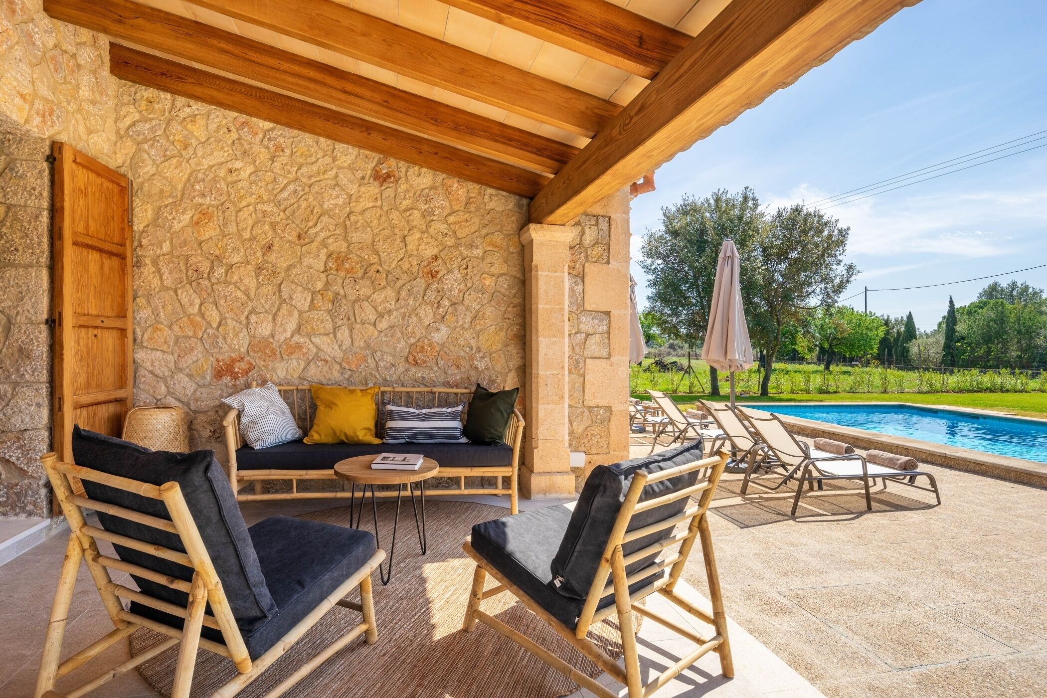 An outdoor seating area with a stone wall, wooden furniture, and a pool.