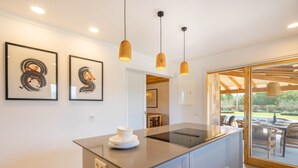 A modern kitchen with a central island, pendant lights, and framed artwork on the wall. - Villa Can Canavaret by SunVillas Mallorca (Pollença)