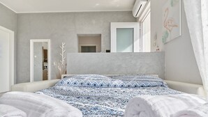 A modern bedroom with a bed, towels, a mirror, and a door. - MINERVA HOLIDAYHOME - MIMOSA APARTMENT (Manerba del Garda)