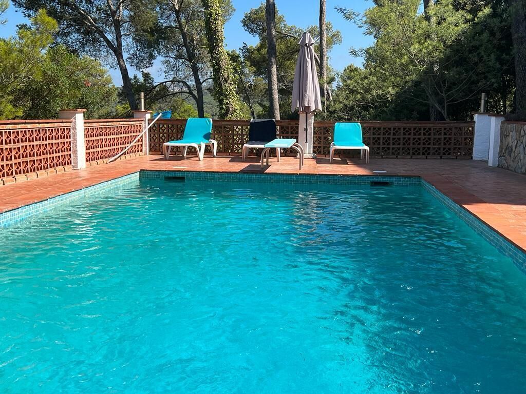 Ein rechteckiger Swimmingpool mit klarem, blauem Wasser, umgeben von einer Holzterrasse. Drei blaue Liegestühle und ein Sonnenschirm befinden sich dort.