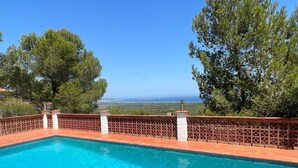 A clear blue swimming pool with a wooden fence and stone pillars, surrounded by trees and a view of the sea. - Villa Pals very beautiful sea view and Medes islands, private swimming pool (Pals - Masos de Pals)