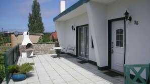 Eine überdachte Terrasse im Freien mit Grill, Tisch und Bank.