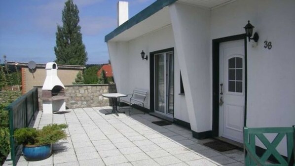 A covered outdoor patio with a barbecue grill, a table, and a bench.
