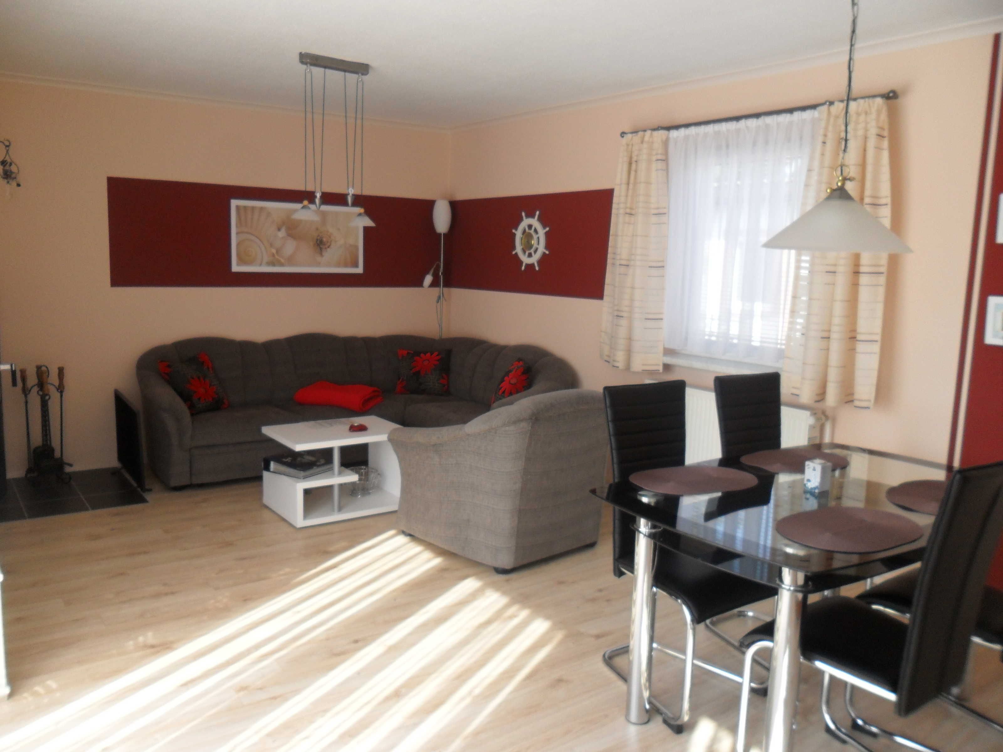 Ein Wohnzimmer mit grauem Sofa, einem weißen Beistelltisch, einem Glastisch mit vier Stühlen und einer Pendelleuchte.