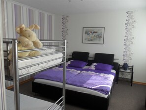 Ein Etagenbett mit einem Teddybären im oberen Bett, ein schwarzer Stuhl, ein kleiner Tisch mit einer Lampe und ein gerahmtes Bild an der Wand.