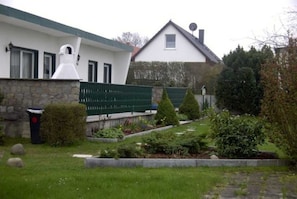A house with a stone wall, a green fence, and a garden with various plants and a small tree.