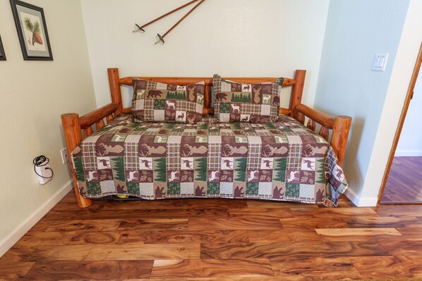 Un divano letto in legno con motivo a cervi trapuntato, posto su un pavimento in legno.
