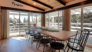 Una larga mesa de comedor de madera con sillas negras, ventanas amplias y un letrero en la pared que dice "Memories".