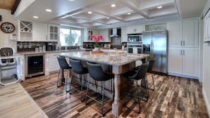 Una cocina amplia con una isla grande, taburetes de bar, muebles blancos y electrodomésticos de acero inoxidable.
