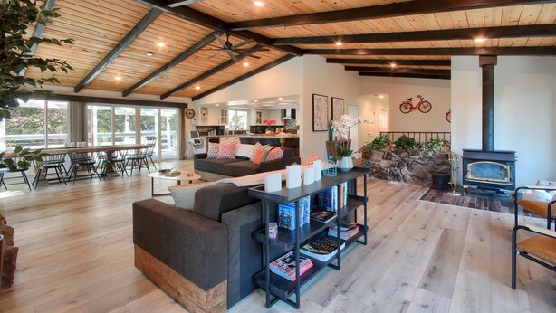 Amplia sala de estar con techo alto, vigas de madera, chimenea y comedor con luz natural.