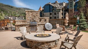 A patio area with a stone fire pit, outdoor furniture, and a view of a mountain.