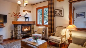 Un salon chaleureux avec une cheminée en pierre, deux fauteuils rembourrés, une table basse, un téléviseur et un grand miroir.
