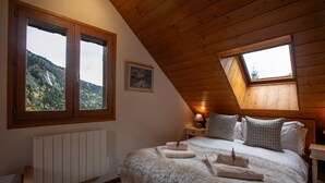 Une chambre avec un plafond en pente, deux fenêtres donnant sur les montagnes, un lit avec une literie moelleuse et une table de chevet avec une lampe.
