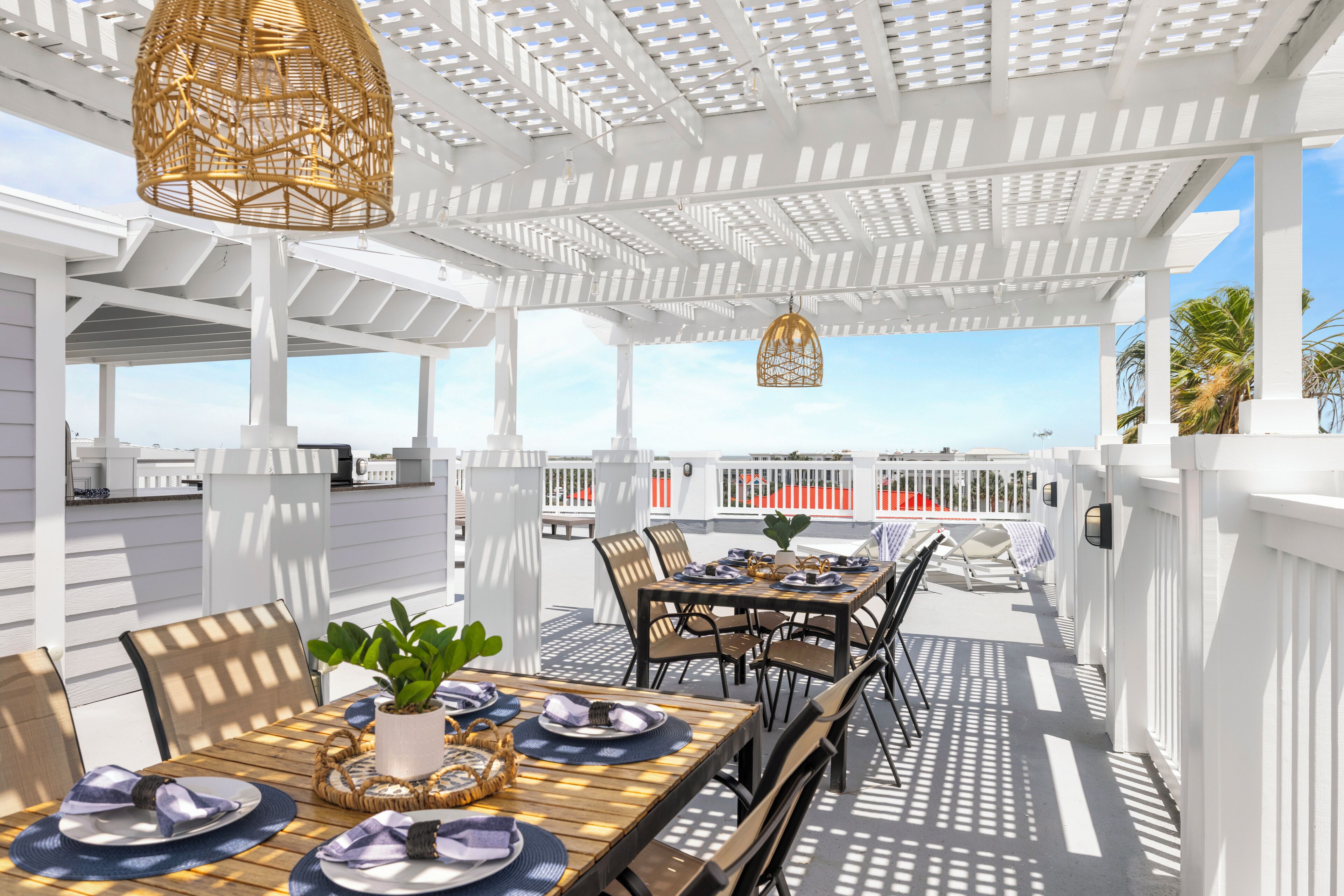 An outdoor patio with white railings, tables set for dining, and hanging wicker lamps.