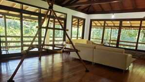 Ein geräumiges Zimmer mit Holzboden, großen Fenstern, einem weißen Sofa und einer Holzleiter-Konstruktion.