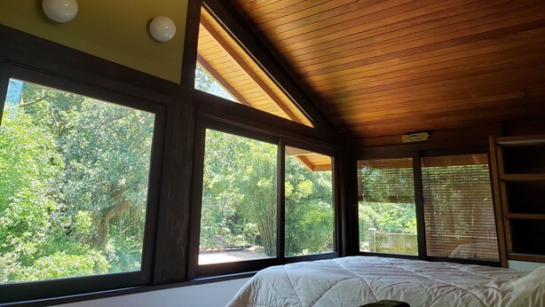 Ein Schlafzimmer mit einem großen Bett, Holzboden und großen Fenstern mit Blick auf Grünflächen.