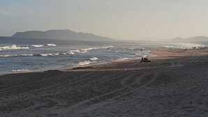 Ein Strand mit Wellen, Menschen und Bergen im Hintergrund.
