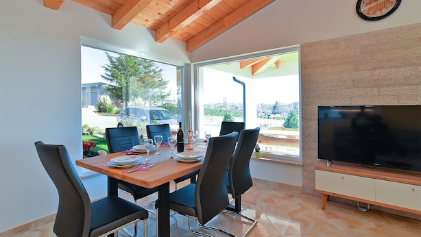 A dining area with a wooden table and chairs, a television, and a large window offering a view of the outdoors. - House 2065/32772 (Istria - Žminj), 20000m from the beach (Žminj)