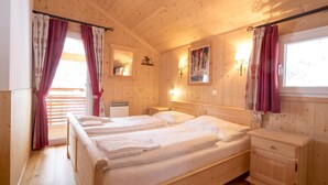 Een slaapkamer in een houten hutje met twee bedden, een nachtkastje en een raam met gordijnen.