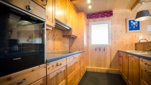 Een keuken met houten kastjes, een Siemens oven, een raam en een spoelbak.