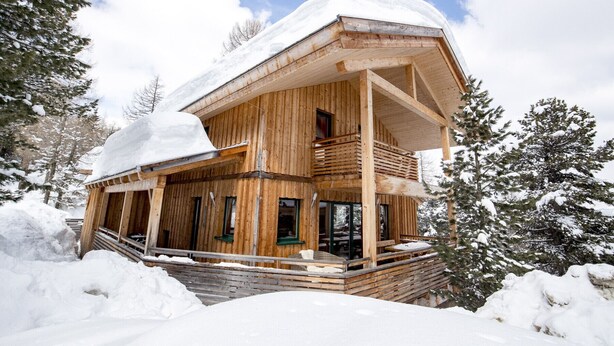Een houten chalet met een balkon, omringd door met sneeuw bedekte bomen.