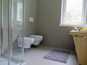 Een badkamer met twee toiletten, een glazen douchecabine, een wastafel met een houten kastje en een raam voor natuurlijk licht.