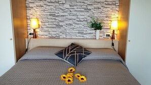 Un lit avec un mur en pierre en arrière-plan, deux lampes de chevet, un coussin décoratif et des tournesols sur le lit.