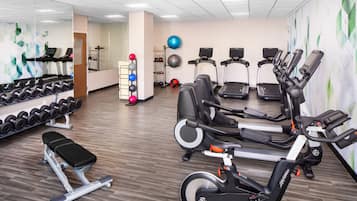 A gym with treadmills, elliptical machines, a bench, and a rack of dumbbells.