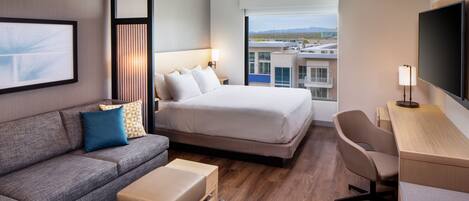 Una habitación de hotel moderna con cama, sofá, escritorio y un ventanal con vistas a la ciudad.