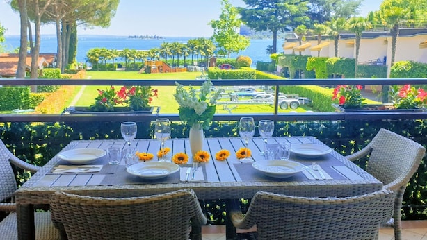 An outdoor dining area with a table set for four, overlooking a landscaped garden and the sea.