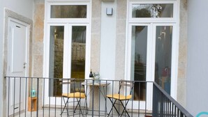 Ein Balkon mit zwei Stühlen, einem Tisch, einer Steinmauer und einer Tür.