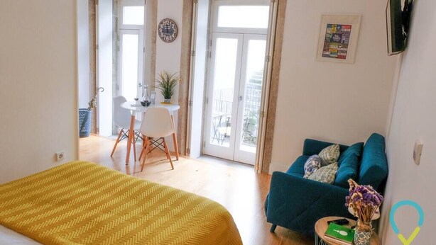 Ein Zimmer mit einem Bett, einem blauen Sofa, einem kleinen Tisch mit einer Vase und einer Tür, die auf einen Balkon führt.