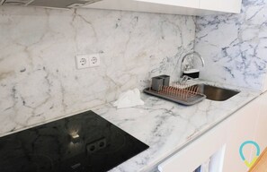 Une cuisine dotée d’un plan de travail en marbre, d’une plaque de cuisson à induction noire, d’un évier avec un robinet et d’une étagère métallique.