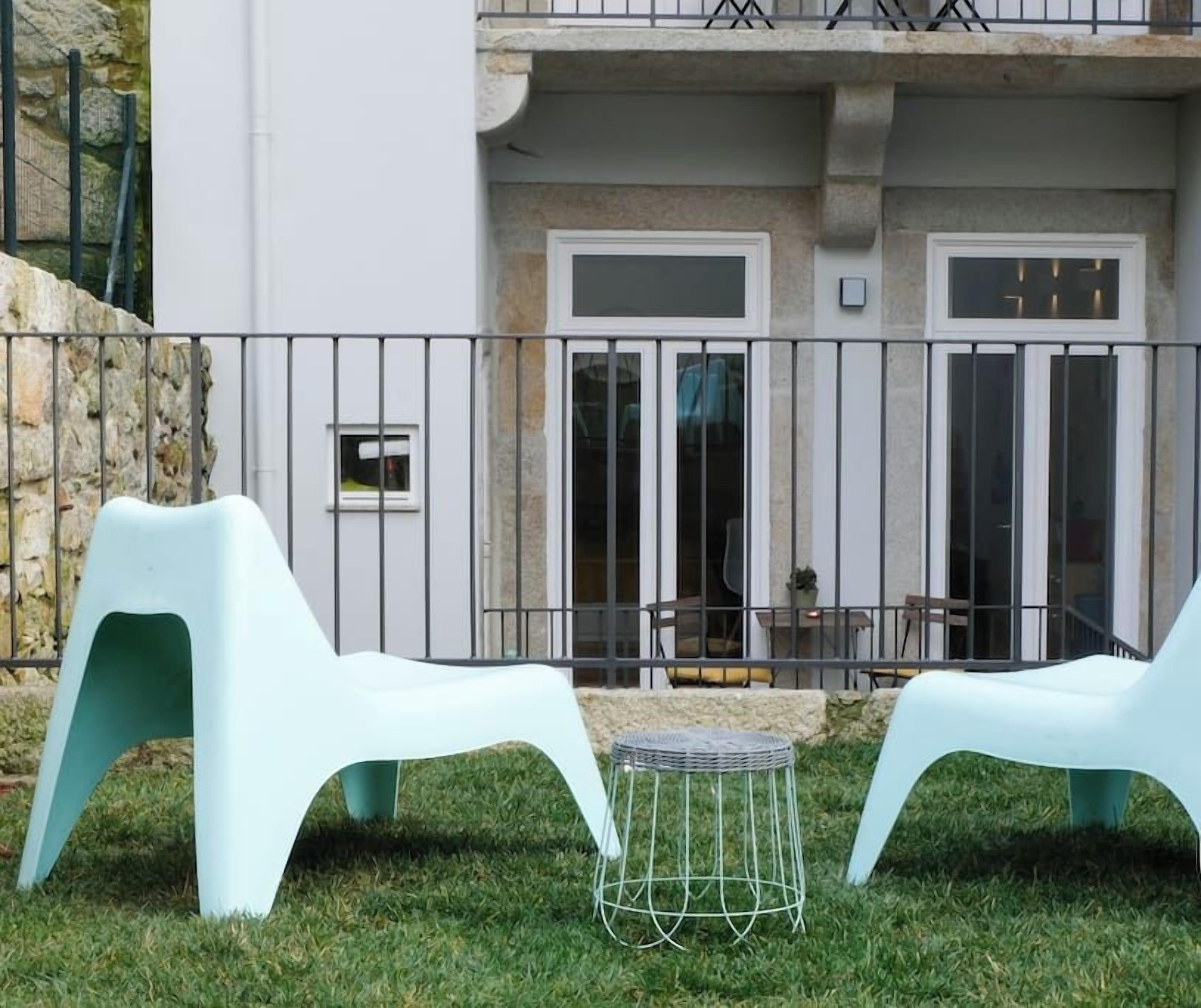 Un espace extérieur aménagé avec deux chaises blanches et une petite table ronde, un mur en pierre et un balcon doté d’une balustrade.