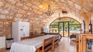 A stone-walled room with a dining table, benches, a refrigerator, and a TV. - Holiday Home “Sa Mina” with Garden, Pool, Terraces, Air Conditioning & WiFi (Selva)