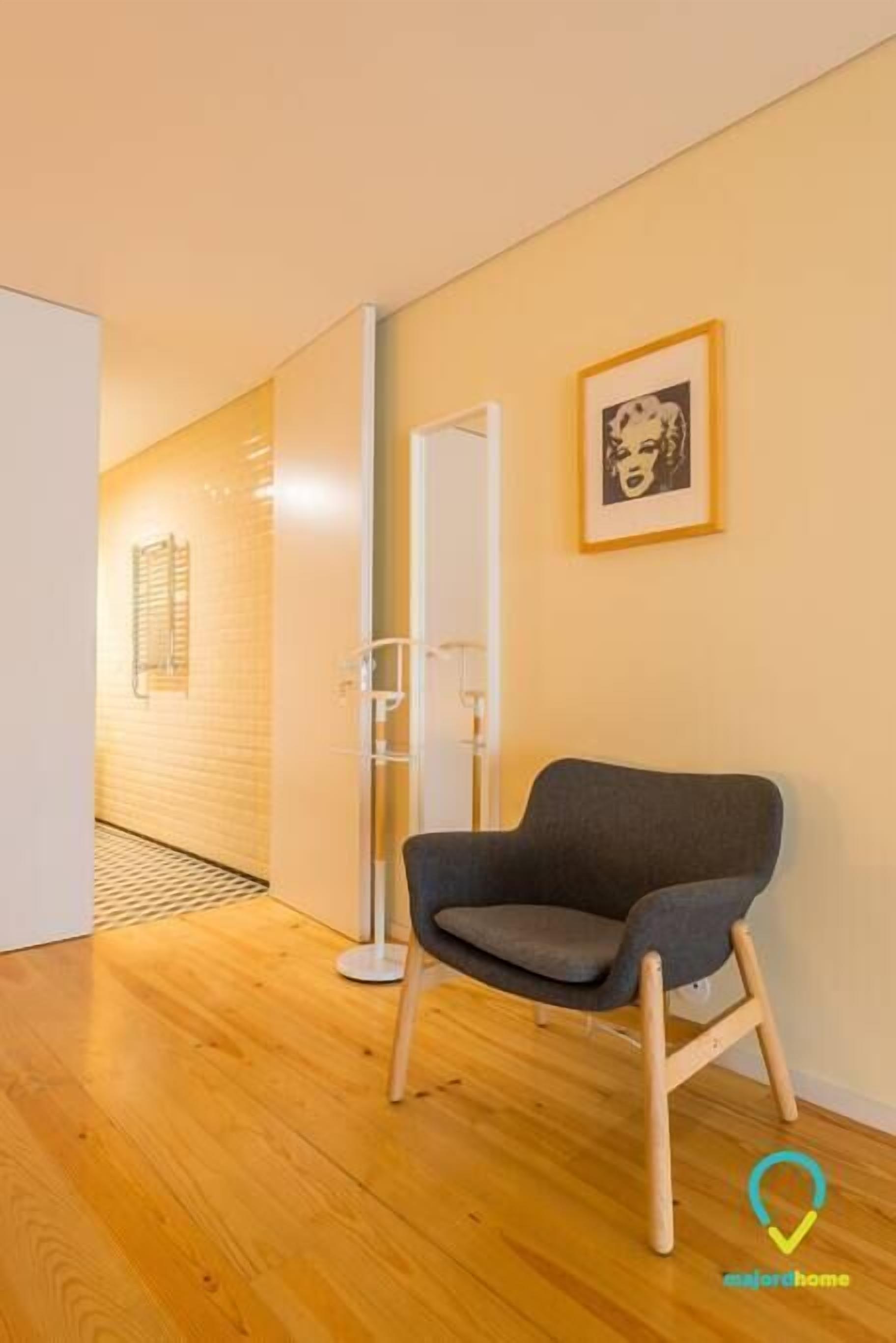 A modern room with a wooden floor, a grey armchair, a white door, and a framed picture on the wall.