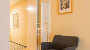 Une pièce moderne avec un plancher en bois, un fauteuil gris, une porte blanche et un tableau encadré au mur.