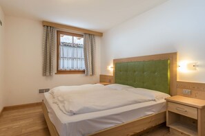 A bedroom with a bed, a nightstand, a window with curtains, and a wall-mounted light.