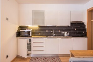 A compact kitchen with white cabinets, a microwave, a sink, and a small table.