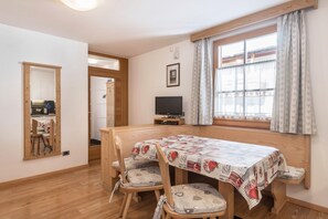 A dining area with a table, chairs, a television, and a window with curtains.
