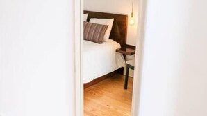 Un dormitorio con un espejo grande, suelo de madera, una cama con almohadas y una lámpara de noche.