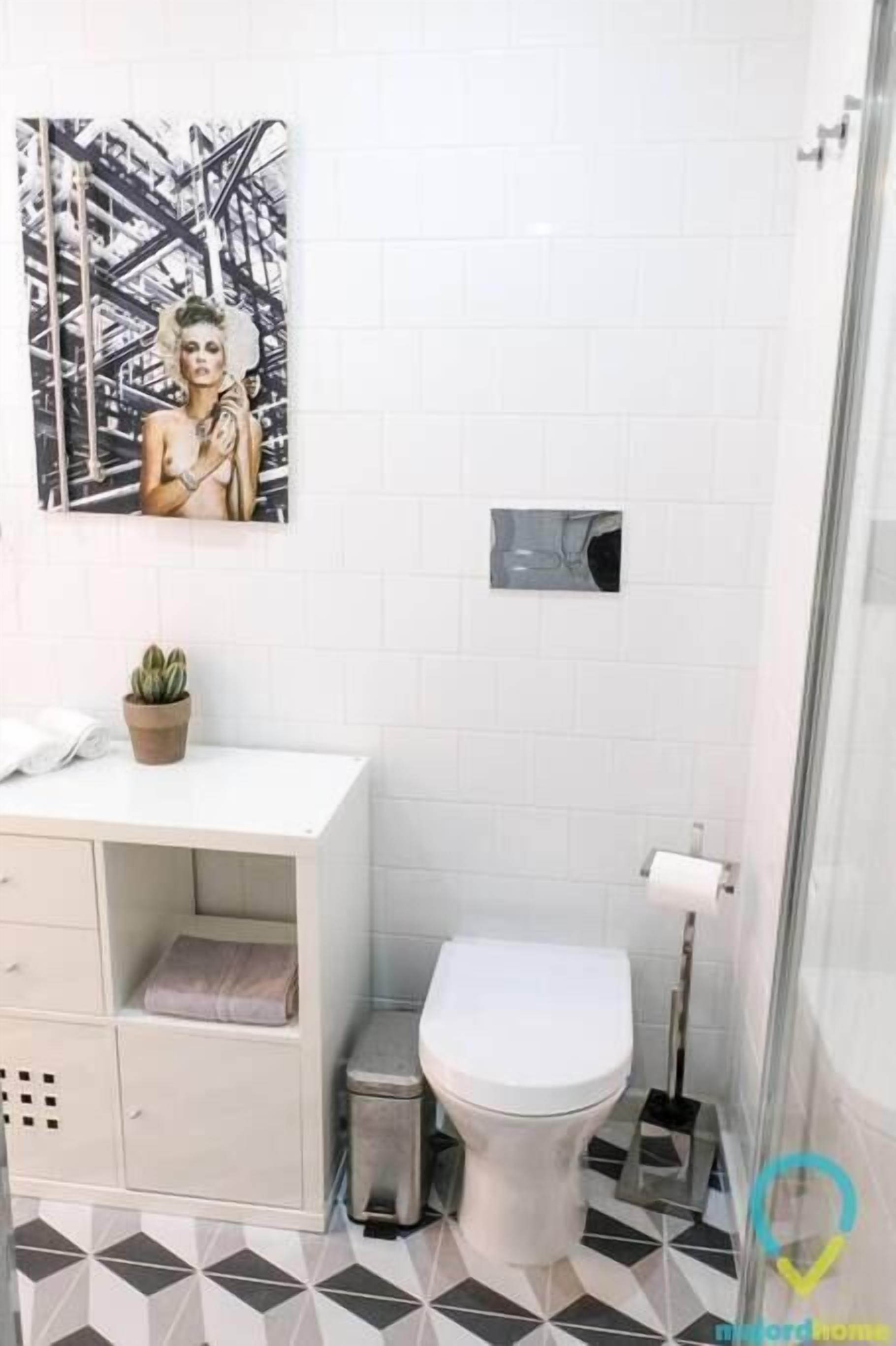 A bathroom with a white toilet, a small trash bin, a sink with a potted plant, and a shower area.
