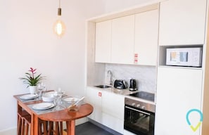 A compact kitchen with white cabinets, a microwave, a stove, and a sink.