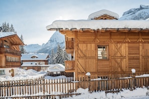 A wooden chalet with a snow-covered roof, surrounded by a wooden fence and snow-covered ground.