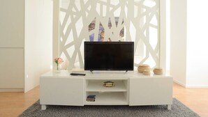 A white entertainment unit with a flat-screen TV, a remote control, and decorative items. - SOFTLY PORTO - Lovely apartment right the heart of city (Porto)