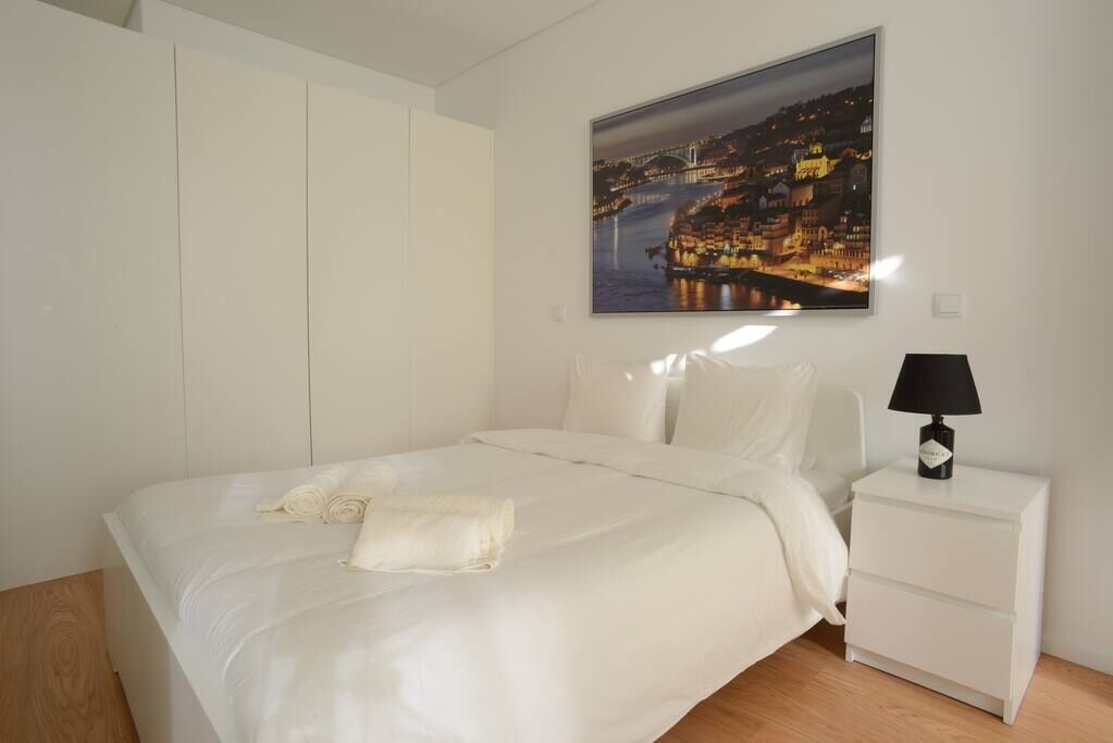 Un dormitorio con una cama, una mesita de noche, una lámpara y un cuadro de un paisaje urbano.