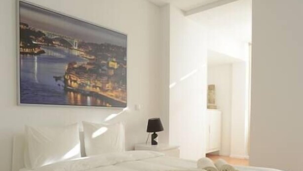 A modern bedroom with a large bed, a nightstand, a lamp, and a painting of a cityscape. - SOFTLY PORTO - Lovely apartment right the heart of city (Porto)