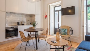 A modern kitchen with white cabinets, a built-in oven, and a dining area with wicker chairs and a round table.