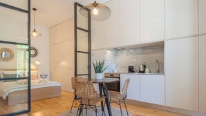 A modern kitchen with white cabinets, a round dining table with wicker chairs, and a potted plant.